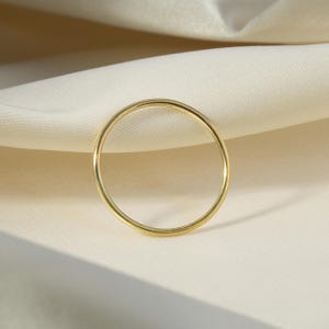 Puede incluir: Un anillo fino de oro con un diseño simple y minimalista. El anillo es circular y parece estar hecho de metal pulido. El anillo está sobre un fondo de tela de color crema.