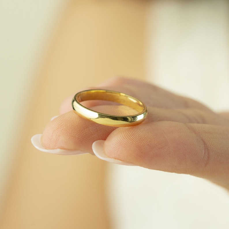 May include: A polished yellow gold band ring with a smooth, rounded surface and a simple, classic design. The ring features a continuous, solid metal construction with a high-shine finish that reflects light across its curved, circular exterior.