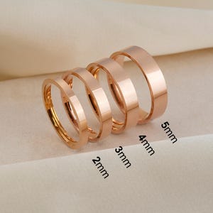 Puede incluir: Cuatro anillos de metal en tono oro rosa dispuestos en fila, cada uno con un ancho de banda diferente. Los anchos están claramente etiquetados como 2mm, 3mm, 4mm y 5mm, indicando la medida específica para cada anillo de este conjunto.