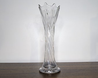 May include: A clear glass vase with a twisted design. The vase has a wide mouth and a narrow base.