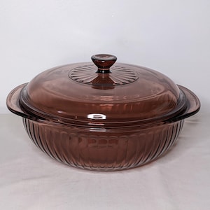 May include: A brown glass casserole dish with a lid. The dish has a ribbed design on the sides and a round lid with a knob. The dish is likely used for baking and serving food.