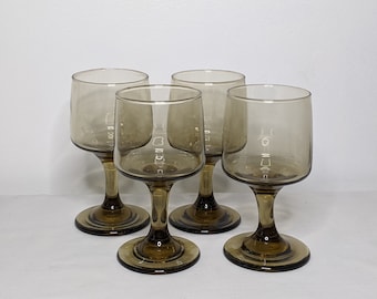May include: Set of four amber-colored wine glasses with a clear glass bowl and a thick stem. The glasses have a rounded bowl and a flared lip.