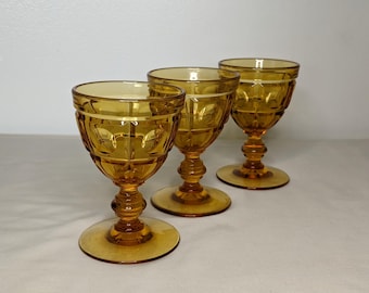 May include: Three amber-colored vintage goblets with a decorative pattern. The goblets have a round base, a stem with a bulbous design, and a patterned bowl. The glasses are made of glass and are suitable for serving beverages.
