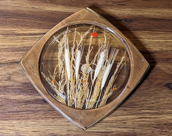 May include: A wooden coaster with a clear resin top featuring dried grasses and a small red ladybug. The coaster is a square shape with rounded corners.