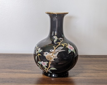 May include: A black ceramic vase with a gold rim and a floral design featuring a bird and pink flowers.