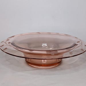 May include: A pink glass pedestal bowl with a delicate etched floral design. The bowl has a wide rim and a raised base.