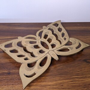 May include: A gold metal butterfly-shaped trivet. The trivet has a decorative design with cutouts.