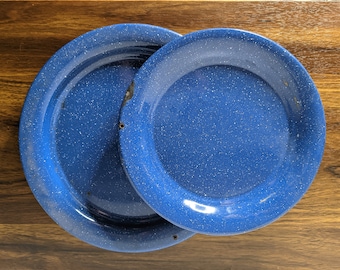 May include: Two blue enamel plates, one stacked on top of the other. The plates have a speckled blue finish and a white rim.