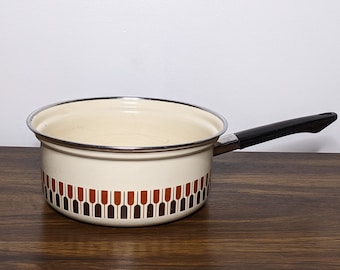 May include: A white enamel saucepan with a black handle. The saucepan has a brown and orange geometric pattern around the bottom.