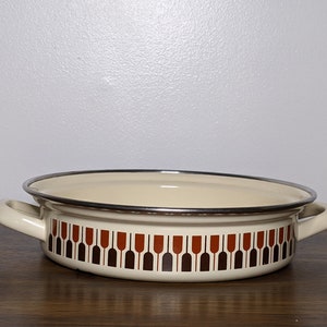 May include: A white enamel baking dish with brown and orange geometric pattern. The dish has two handles and a silver rim.