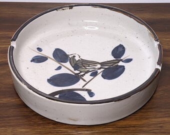 May include: A white ceramic ashtray with a brown rim and a blue and brown bird design.