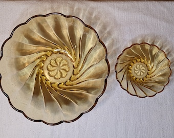 May include: Two amber-colored glass bowls with a spiral design. The larger bowl is approximately 9 inches in diameter, and the smaller bowl is about 5 inches across. Both have a scalloped edge and a floral design in the center.