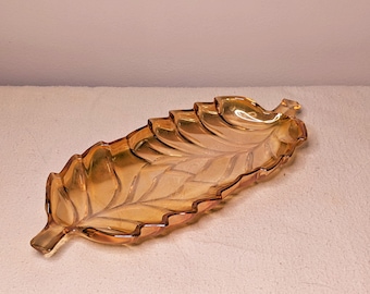 May include: Amber glass leaf-shaped serving dish. The dish has a wavy edge and a detailed leaf design.