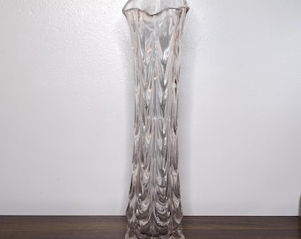 May include: A tall, clear glass vase with a textured, wave-like pattern. The vase has a flared, scalloped rim and a slender, elongated body. The vase is approximately 12 inches tall.