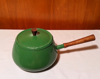 May include: Green enamel fondue pot with a wooden handle and lid. The pot is round and has a wide base.