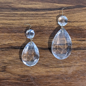 May include: Two clear glass teardrop-shaped crystal prisms with faceted edges, each hanging from a gold-colored wire.