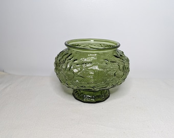 May include: A green glass vase with a textured surface and a wide base. The vase is perfect for displaying flowers or other decorative items.