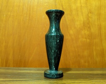 May include: A small, dark green marble vase with a simple, elegant design. The vase has a round base and a narrow neck.
