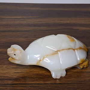 May include: White onyx turtle figurine with brown veining. The turtle is carved in a realistic style with a detailed shell and head.