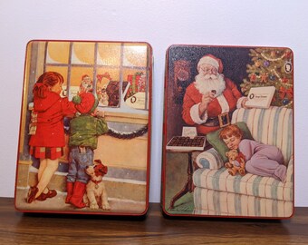 May include: Two rectangular vintage Christmas tins. One tin features children looking at a shop window with gifts. The other tin shows Santa Claus and a sleeping child. Both tins have a red border.