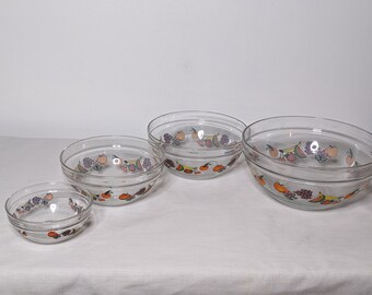 May include: Set of four clear glass bowls with a fruit design. The bowls are nested inside each other, with the largest bowl at the bottom and the smallest bowl at the top. The fruit design features oranges, cherries, bananas, and watermelons.