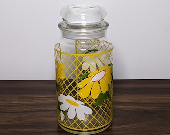 May include: A clear glass jar with a yellow and white floral design. The jar has a lid and is decorated with a yellow lattice pattern.