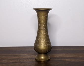 May include: A brass vase with an intricate floral design. The vase has a wide mouth and a narrow base.