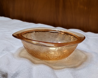 May include: A small, amber-colored glass bowl with a floral pattern. The bowl has a slightly scalloped rim and is sitting on a white surface.