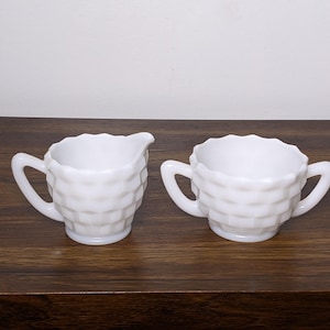 May include: A white milk glass creamer and sugar bowl set with a textured, diamond-shaped pattern.