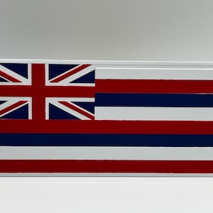 Puede incluir: Un letrero rectangular blanco con una imagen en relieve del emblema del estado de Hawái. La bandera presenta una Union Jack roja, blanca y azul en la esquina superior izquierda y ocho rayas rojas y blancas alternas.