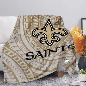 May include: A brown and white throw blanket with a gold fleur-de-lis and the word "Saints" in black lettering. The design is a tribal pattern.