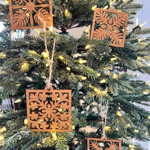 May include: Four wooden ornaments with intricate cut-out designs hang on a Christmas tree. The ornaments are brown and feature a variety of geometric patterns.