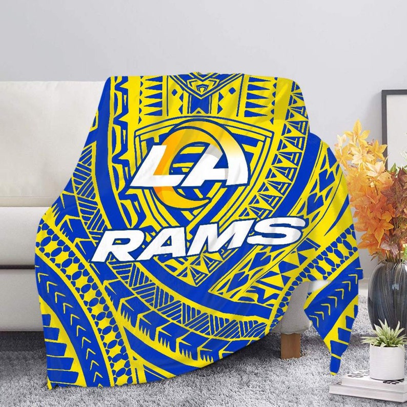 May include: A blue and yellow throw blanket with a tribal pattern and the Los Angeles Rams logo. The logo features the letters "LA" in a white circle with a yellow outline, and the word "RAMS" in white letters below the circle.