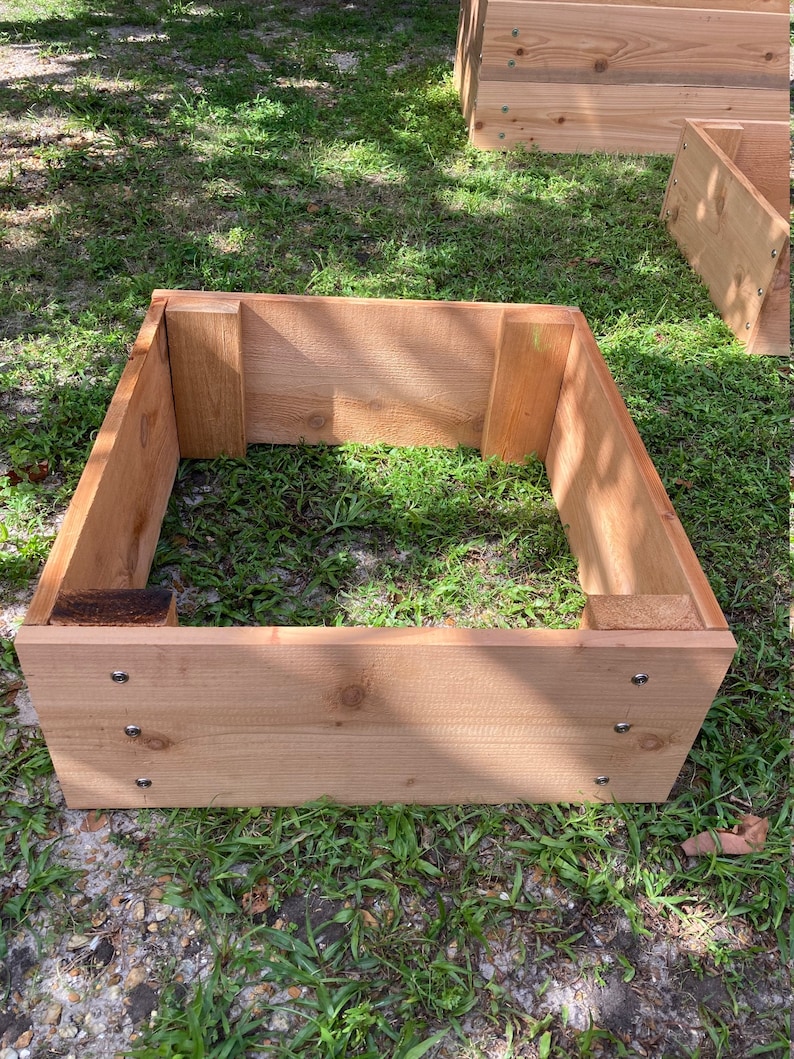 May include: A wooden raised garden bed made of cedar planks. The bed is assembled and ready for planting. The bed is sitting on a grassy lawn.