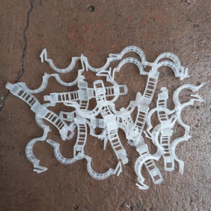 May include: A pile of white plastic plant supports, also known as plant ties or plant clips, used to help support growing plants.