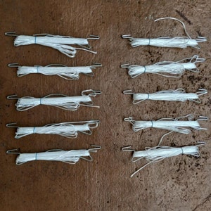 May include: Ten rolls of white string with metal hooks on each end. The string is coiled and tied together with a blue rubber band.