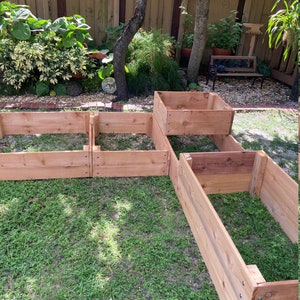 May include: Four wooden raised garden beds in a backyard setting. The beds are made of cedar wood and are arranged in a staggered pattern. The beds are surrounded by green grass.