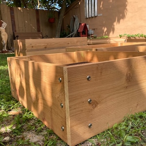 May include: A close-up of a wooden raised garden bed made of cedar planks. The bed is assembled with screws and has a natural wood finish.