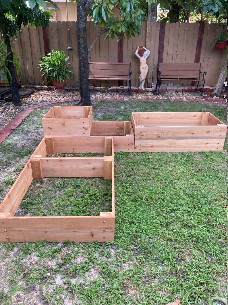 May include: Four wooden raised garden beds in various sizes, assembled in a backyard setting. The beds are made of natural cedar wood and are ready for planting.