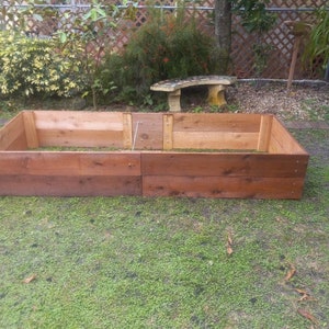 May include: A raised garden bed made of cedar wood with two sections. The bed is empty and ready for planting. The bed is sitting on a green lawn.