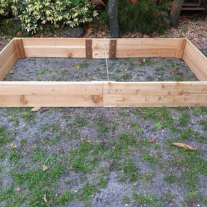 May include: A wooden raised garden bed with two sections, made of untreated cedar planks. The bed is empty and ready for planting.