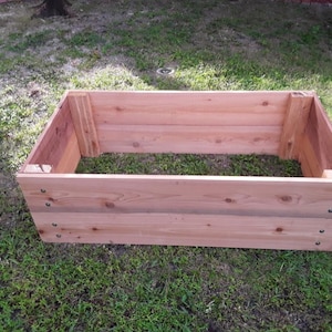 May include: A rectangular wooden raised garden bed made of cedar planks. The bed is assembled with screws and has a natural wood finish.