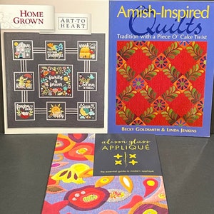 May include: Three quilting books with colorful covers. The first book is titled "Home Grown Art to Heart" and features a quilt block with various phrases. The second book is titled "Amish-Inspired Quilts Tradition with a Piece O' Cake Twist" and features a red quilt with green and yellow accents. The third book is titled "Alison Glass Applique The Essential Guide to Modern Applique" and features a colorful applique quilt design.