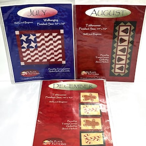 May include: Three quilting pattern packets. The "July" packet is blue with a red, white, and blue flag design. The "August" packet is red with a geometric design. The "December" packet is red with gingerbread men and candy cane designs.