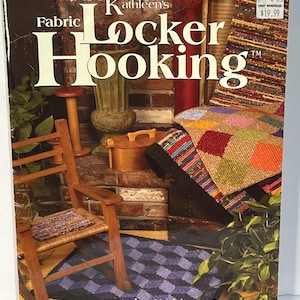 May include: A softcover instructional book titled Kathleen's Fabric Locker Hooking by Kathleen Carpenter. The cover features a wooden rocking chair with a multi-colored fabric seat, a purple checkered rug, and various fabric-hooked textile projects.