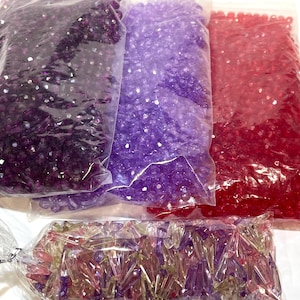 Peut inclure: Quatre sachets de perles de verre assorties. Les sachets contiennent des perles violettes, violettes claires, rouges et transparentes irisées.