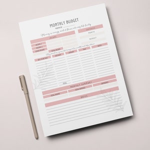 K&ouml;nnte beinhalten: Ein druckbarer monatlicher Budgetplaner mit einem rosa-grauen floralen Design. Der Planer enth&auml;lt Abschnitte f&uuml;r Einnahmen, Ausgaben und eine monatliche Zusammenfassung. Der Text "Geld ist Energie und es flie&szlig;t frei in mein Leben" steht oben auf der Seite.
