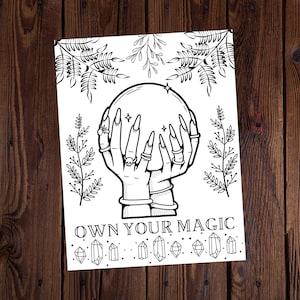 May include: Black and white illustration of hands holding a crystal ball, with long nails and rings. The image includes the text "OWN YOUR MAGIC" and decorative crystals and foliage. The artwork is on a white background.