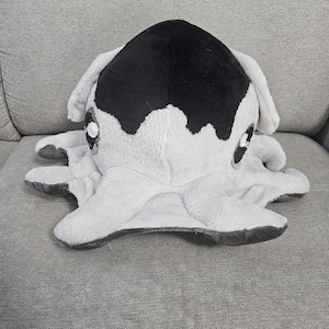 May include: A plush octopus toy in white and black. The toy has large, round eyes and eight tentacles. The top of the octopus is black, and the rest of the body is white. The toy is soft and cuddly.