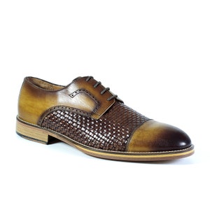 Puede incluir: Zapatos de vestir de cuero marr&oacute;n con un patr&oacute;n tejido en la puntera y cierre de cordones.